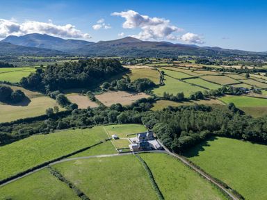 A rural landscape with green fields a house and mountains in the background at Rynys in Llanddeiniolen near Llanrug
