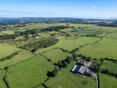 An aerial view of farmland with fields separated by hedges and a barn at Rynys in Llanddeiniolen near Llanrug