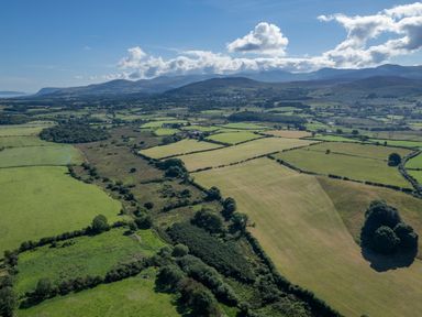 Aerial view of farmland fields with scattered trees and hills in the distance at Rynys in Llanddeiniolen near Llanrug