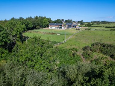 A house with large fenced green lawns surrounded by trees and fields at Rynys in Llanddeiniolen near Llanrug