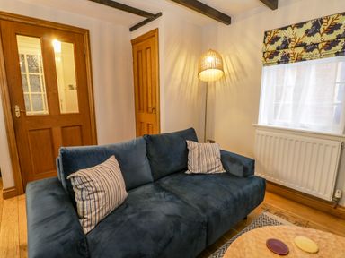 A living room with a blue sofa and striped cushions a wooden door a floor lamp and a window with patterned blinds at April Cottage in Whitby
