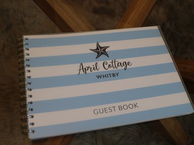 A guest book with blue and white stripes and a starfish graphic on a wooden surface at April Cottage in Whitby