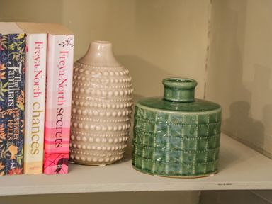 A shelf with three books and two ceramic vases one beige and one green at April Cottage in Whitby