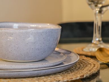 A close up of stacked ceramic bowl and plates on a woven placemat with a wine glass and golden spoon nearby at April Cottage in Whitby