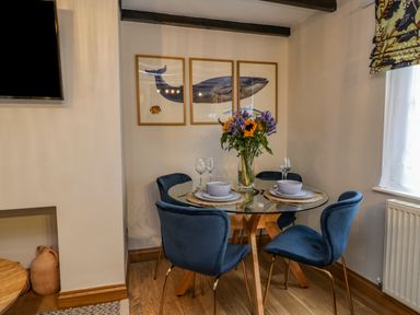 A dining area with a round glass table and four blue chairs with framed whale artwork on the wall at April Cottage in Whitby