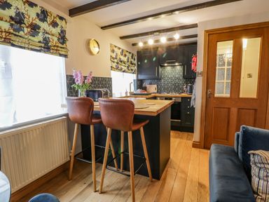 A kitchen area with two brown bar stools at a wooden counter and patterned window blinds at April Cottage in Whitby