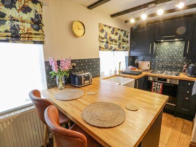 A kitchen with wooden countertops two bar stools a sink oven and patterned window blinds at April Cottage in Whitby
