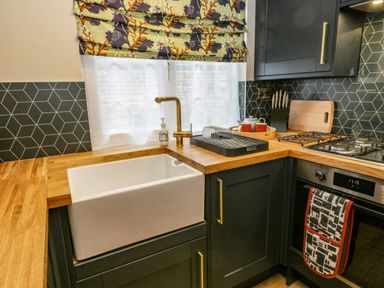 A kitchen with a farmhouse sink wooden countertops black cabinets and a gas stove at April Cottage in Whitby