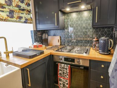 A kitchen with black cabinets wooden countertops gas stove oven and kitchen utensils at April Cottage in Whitby