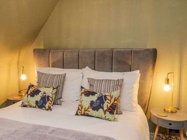 A bedroom with a bed with gray headboard striped and patterned pillows and two bedside tables with lamps at April Cottage in Whitby