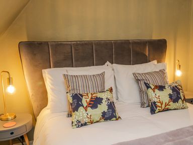 A bedroom with a bed with a gray upholstered headboard two bedside tables with lamps and decorative pillows at April Cottage in Whitby