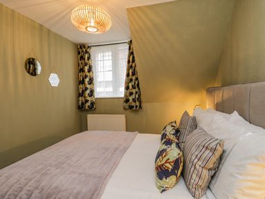 A bedroom with a bed with pillows and a blanket a window with curtains two small wall mirrors and a ceiling light at April Cottage in Whitby