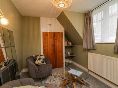 A small sitting room with two grey armchairs a round glass coffee table and a wooden cabinet with shelves at April Cottage in Whitby