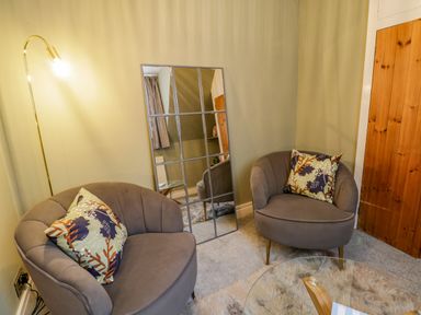 A corner with two armchairs with patterned cushions a floor lamp a grid mirror a glass table and a wooden door at April Cottage in Whitby