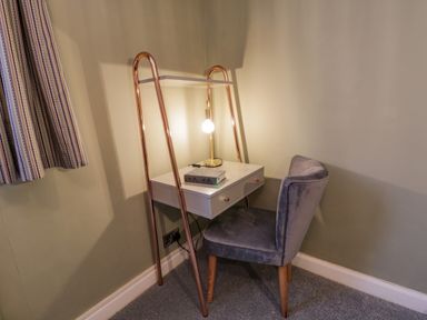 A small desk with a lamp and a book and a chair against a wall with a striped curtain nearby at April Cottage in Whitby