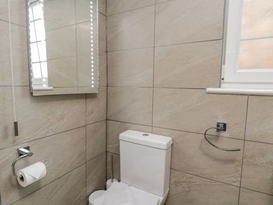 A bathroom with a toilet a roll of toilet paper on a holder a mirror and a window at April Cottage in Whitby