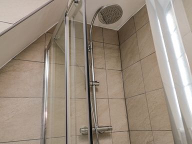 A tiled shower area with a metal showerhead and glass door at April Cottage in Whitby