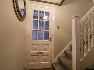 A hallway with a white panel door with glass panes a round wall mirror and a staircase with carpeted steps at April Cottage in Whitby