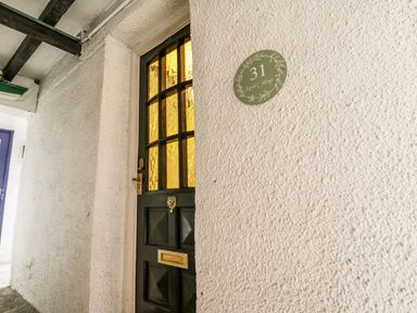 A black door with textured glass panels and a brass mail slot next to a wall with a round green sign labeled 31 April Cottage at April Cottage in Whitby