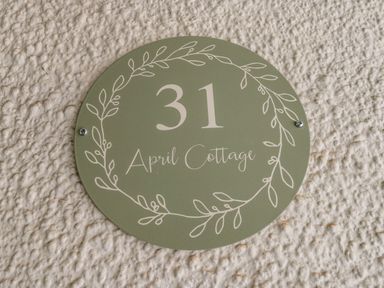 A round green house number sign with the number 31 and text April Cottage on a textured white wall at April Cottage in Whitby