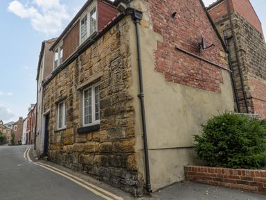 A street corner with a stone and brick building and a small bush at April Cottage in Whitby