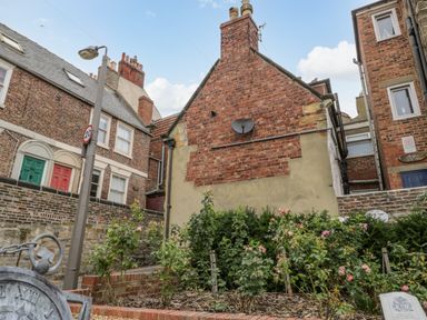 A brick house with a garden of flowers and bushes and a streetlamp with a 20 speed limit sign at April Cottage in Whitby