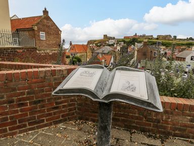 An outdoor metal book display with text and illustrations overlooking houses and a castle on a hill