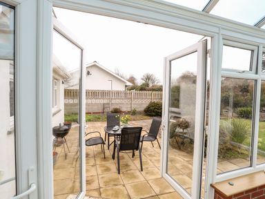 A patio with a table and four chairs and a barbecue grill outside a conservatory at Bro Mebyd in Criccieth
