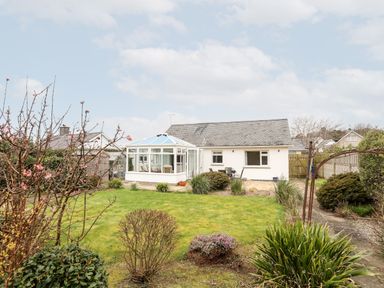 A backyard garden with grass lawn bushes and a conservatory attached to a single story house at Bro Mebyd in Criccieth