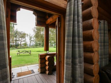 View from inside a wooden log cabin looking out to a grassy area with a picnic table at Brynallt Country Park Frankton near Ellesmere