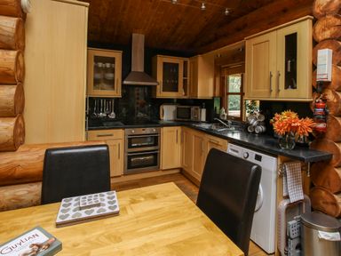 A kitchen with wooden cabinets black countertops a dining table with black chairs flowers on the counter and kitchen appliances at Brynallt Country Park in Frankton near Ellesmere