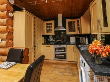 A kitchen with wooden cabinets and ceiling black countertops and a dining table with black chairs at Brynallt Country Park Frankton near Ellesmere