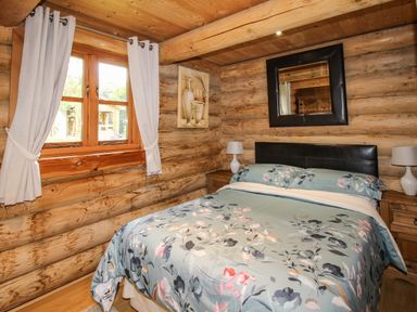 A bedroom with a double bed floral bedding wooden log walls and a window with curtains at Brynallt Country Park Frankton near Ellesmere