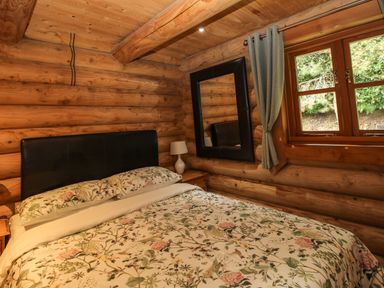 A bedroom with a floral bedspread a black headboard a wooden nightstand a lamp a large mirror and a window with grey curtains at Brynallt Country Park Frankton near Ellesmere