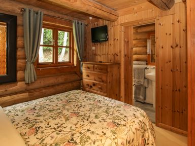 A bedroom with floral bedspread wooden walls window with curtains chest of drawers and a doorway to a bathroom at Brynallt Country Park Frankton near Ellesmere