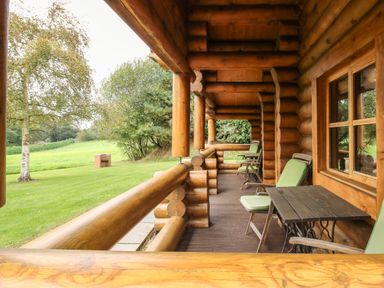 A wooden porch with green cushioned chairs and a table overlooking a grassy area with trees at Brynallt Country Park Frankton near Ellesmere