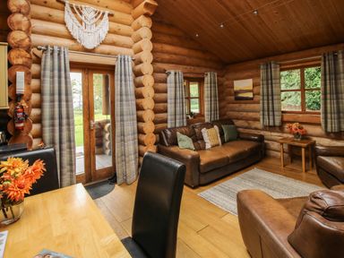 A living room with leather sofas a wooden table with flowers plaid curtains and wooden log walls at Brynallt Country Park Frankton near Ellesmere