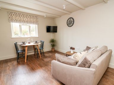 A dining table with two chairs near a window and a sofa with cushions in a living room at Llygad Y Dydd in Bow Street Wales