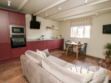 An open plan kitchen and living area with burgundy cabinets a dining table with two chairs and a beige sofa at Llygad Y Dydd in Bow Street Wales