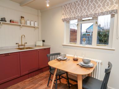 A kitchen with red cabinets a wooden table set for two and a window with patterned blinds at Llygad Y Dydd in Bow Street Wales