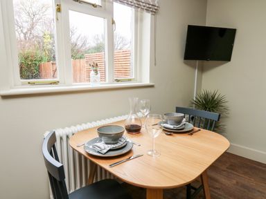A dining area with a wooden table set for two with plates bowls glasses and cutlery next to a window and a wall-mounted TV at Llygad Y Dydd in Bow Street Wales