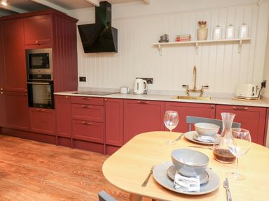 A kitchen with red cabinets a wooden table set with dishes and wine glasses at Llygad Y Dydd in Bow Street Wales
