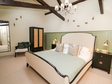 A bedroom with a bed white and black frame bedside tables lamps a black wardrobe chair mirror and ceiling beams at Llygad Y Dydd in Bow Street Wales