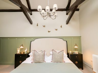 A bedroom with a large bed with pillows two bedside tables with lamps and decorations and a chandelier at Llygad Y Dydd in Bow Street Wales