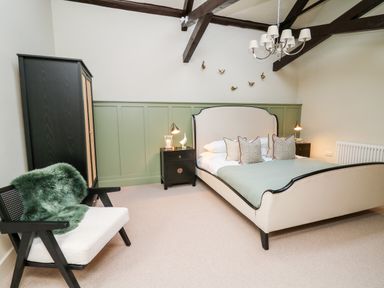 A bedroom with a bed table lamps an armchair and a wardrobe at Llygad Y Dydd in Bow Street Wales