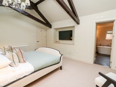 A bedroom with a bed and pillows a wall mounted television and a bathroom visible through an open door at Llygad Y Dydd in Bow Street Wales