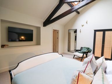 A bedroom with a bed pillows chair mirror wardrobe and a wall mounted TV at Llygad Y Dydd in Bow Street Wales