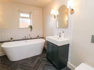 A bathroom with a bathtub sink with cabinet mirror and wall lights at Llygad Y Dydd in Bow Street Wales