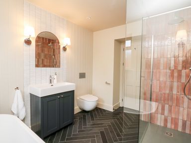 A bathroom with a sink cabinet and mirror a wall-mounted toilet and a glass shower enclosure at Llygad Y Dydd in Bow Street Wales