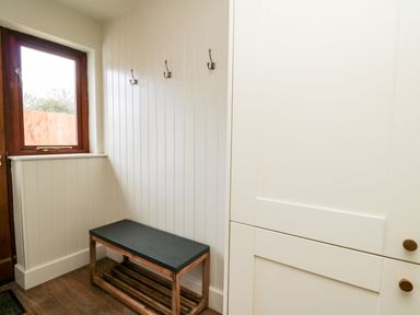 A small entryway with a wooden bench a window hooks on the wall and a white cabinet at Llygad Y Dydd in Bow Street Wales